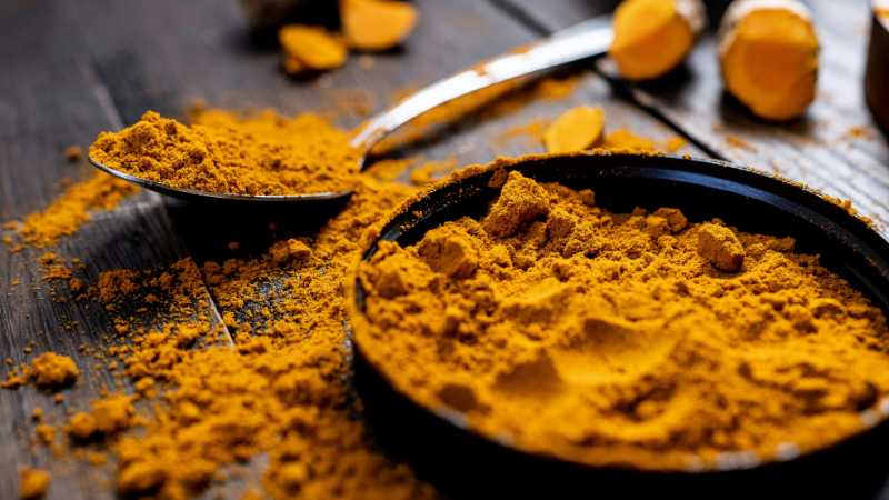 Close-up of vibrant turmeric powder with root on rustic wooden table, emphasizing texture and color., tags: von ein für strahlende - pexel